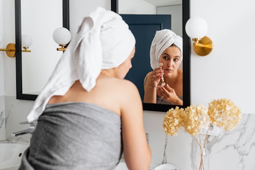 Free A Woman Using a Face Roller in Front of a Wall Mirror Stock Photo
