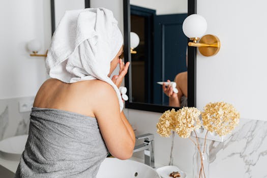 Woman in towel applies skincare in elegant bathroom with modern design, adding to her beauty routine.