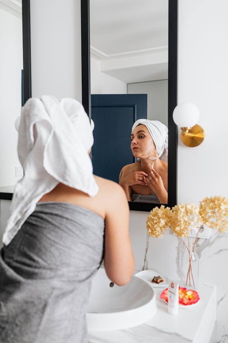 A Woman Using A Face Roller On Her Neck In Front Of A Mirror