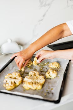 在厨房里，将调味的烤花椰菜片双手放在烤盘上