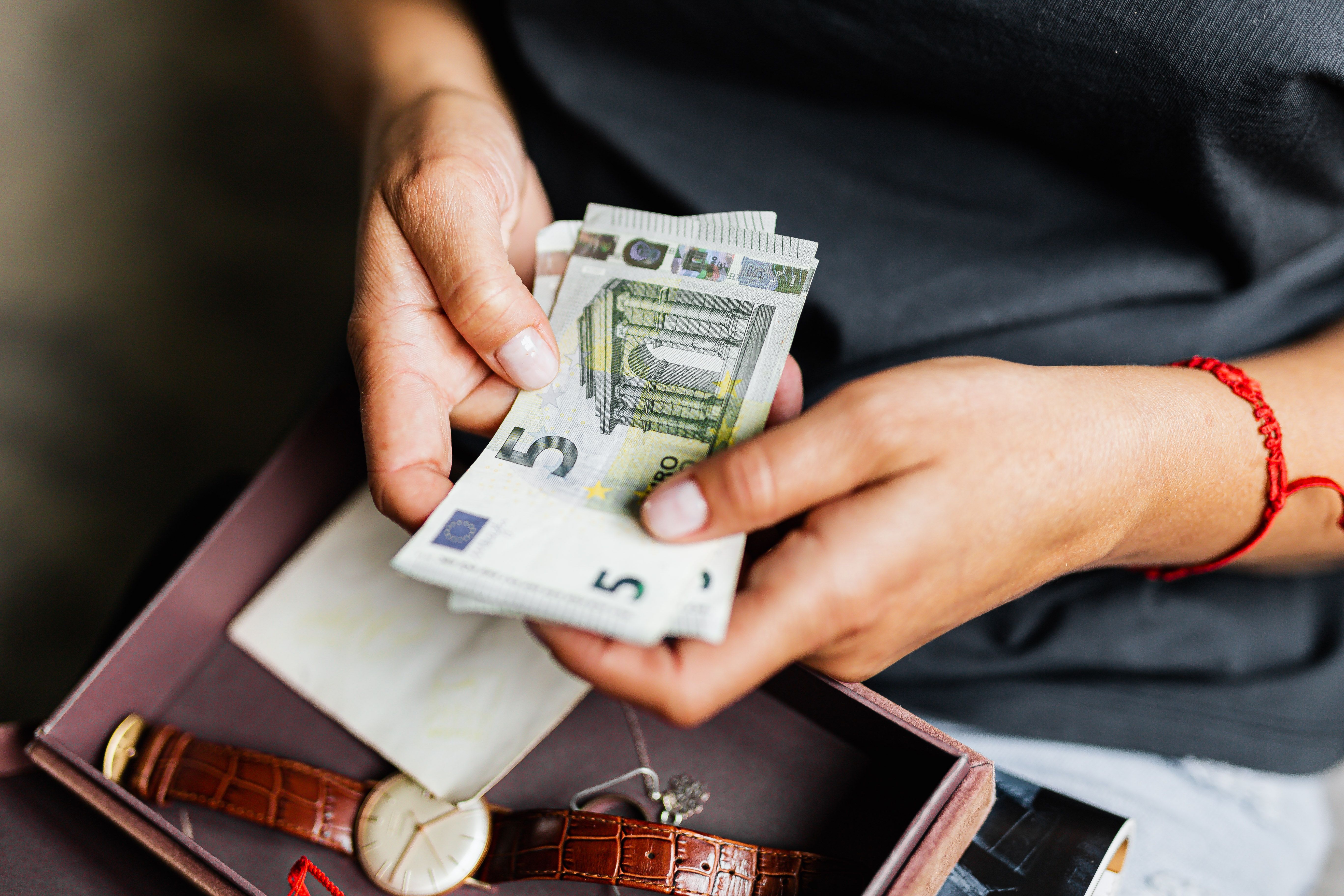 Person counts euro banknotes while holding them above an open box with personal belongings