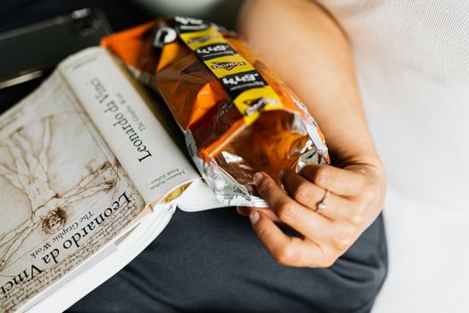 A close-up of a hand with an engagement ring holding a snack packet on a book.