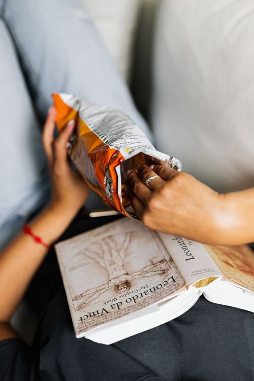 Free Close-up of a person enjoying a snack while reading a book indoors. Stock Photo