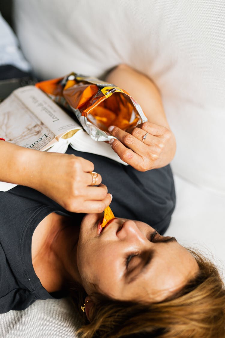 A Woman Lying In Bed Eating A Snack