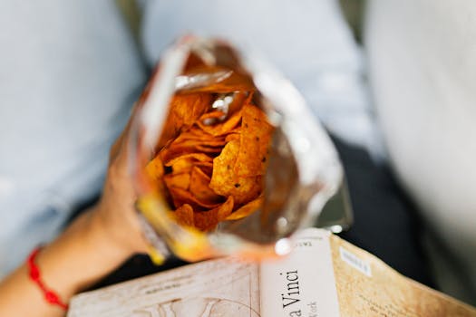 Close-up view of nacho chips inside an open bag held by a person, conveying a casual snacking moment.