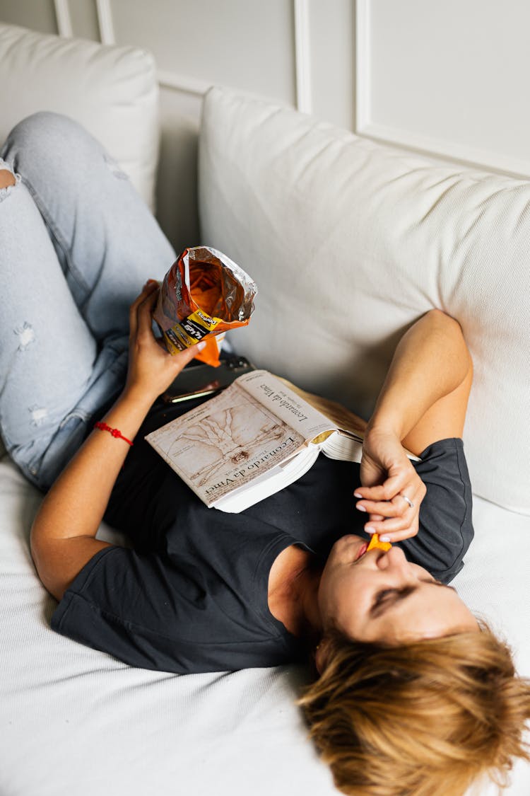 Woman Lying On Bed Eating Chips