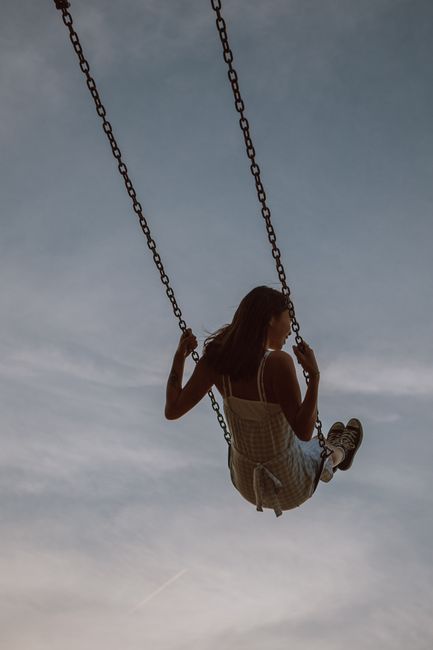 Back view full body of unrecognizable female pushing swing while resting at daytime under blue sky