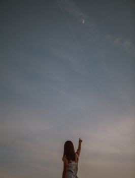 一个女人指着暮色天空中宁静的月亮，唤起和平与自由的感受