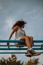 Woman in White Tank Top and Black and White Striped Shorts Sitting on Blue Metal Railings