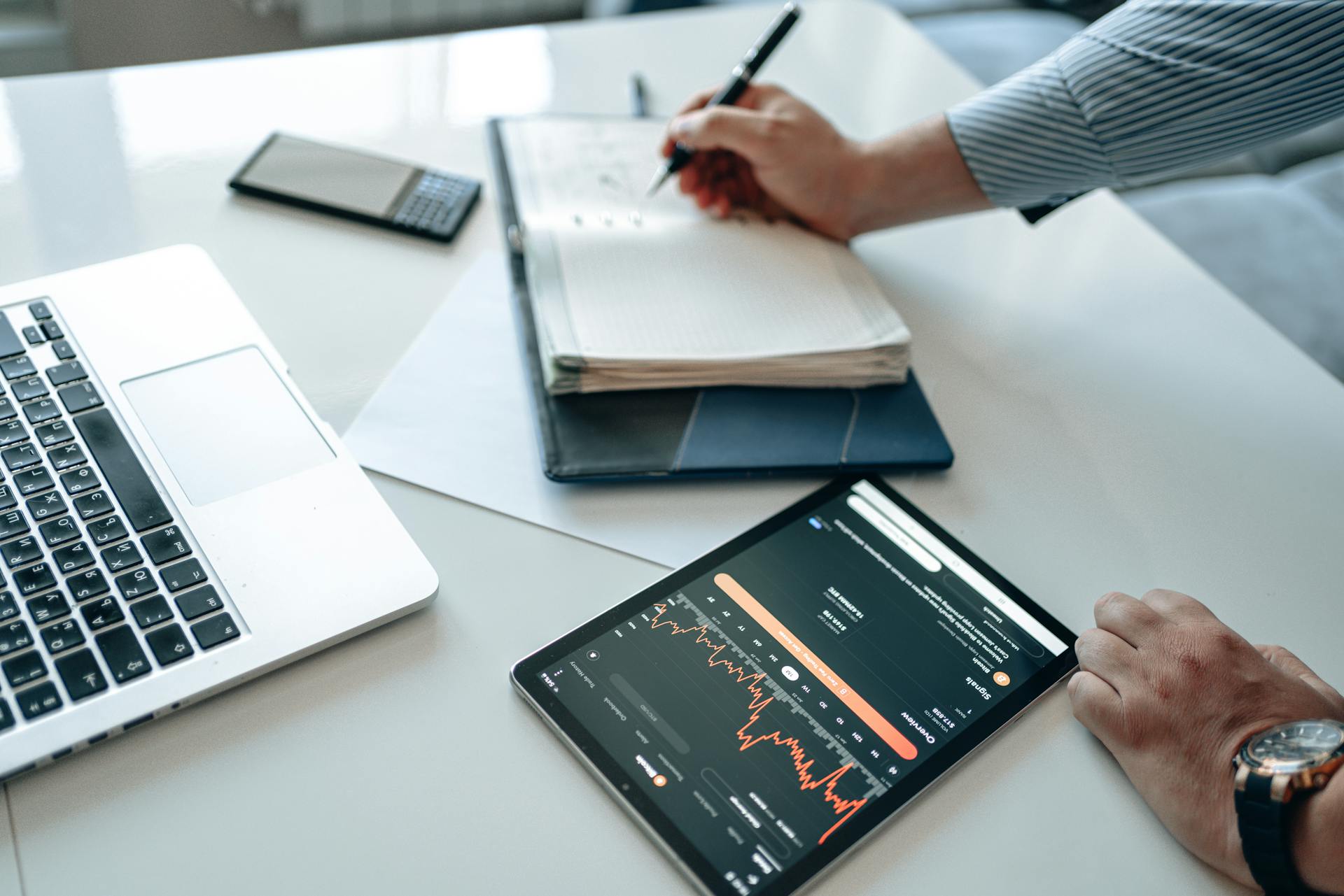 Close-up of a business professional analyzing data trends using a tablet and laptop.