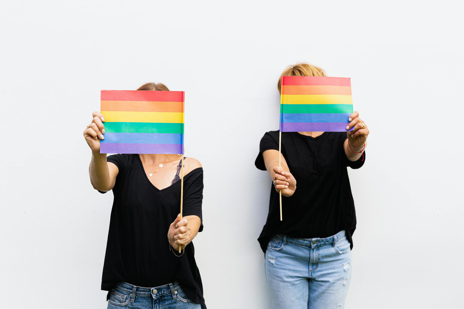 Two women holding rainbow flags covering their faces, symbolizing pride and unity.