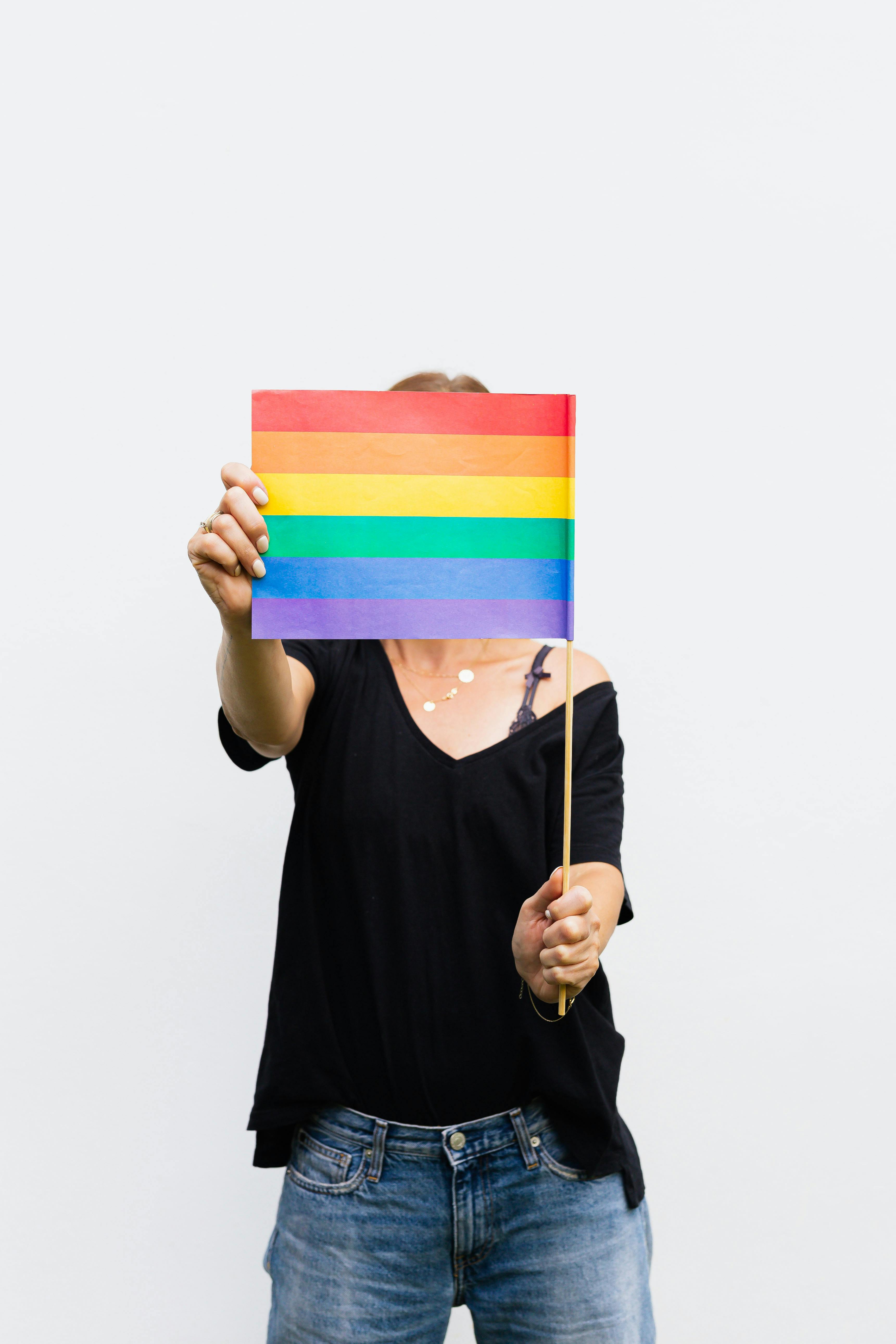 woman in black shirt and blue denim jeans holding a rainbow flag