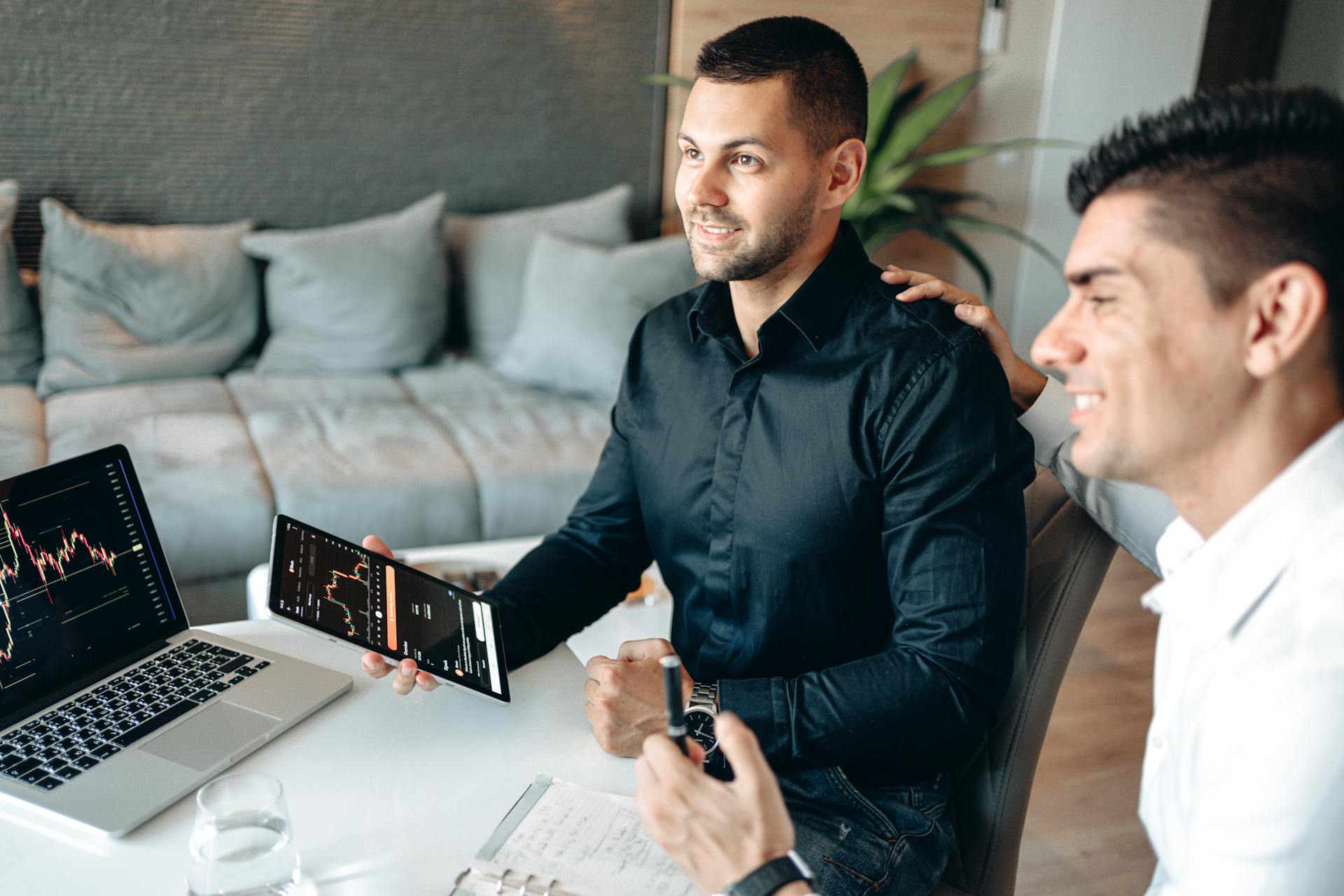 Two businessmen analyzing stock market data on a tablet in a modern office setting.