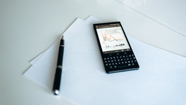 A smartphone displaying graphs placed on white paper with a pen on a table.