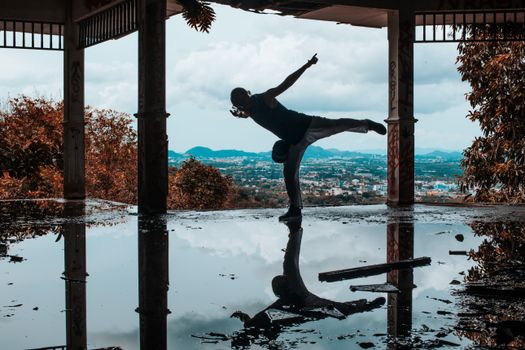 Artistic silhouette of a dancer performing a pose in an urban setting with water reflections.