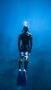 Back view of anonymous diver in oxygen mask and flippers rising from bottom of blue ocean in tropical resort in summer
