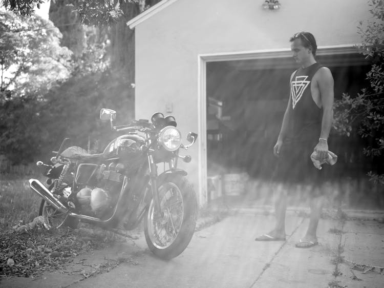 A Man Standing Near A Motorcycle On A Driveway