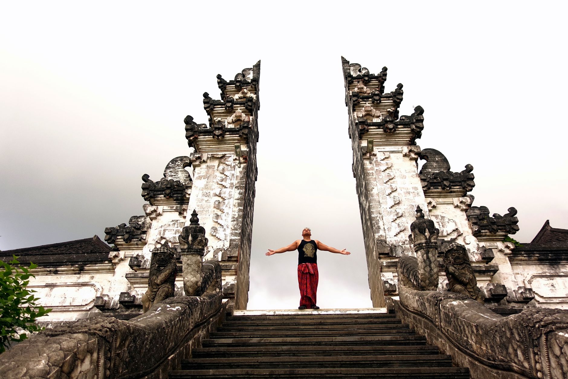 A man stands with arms outstretched at Pura Lempuyang temple in Bali, Indonesia, highlighting its grand architecture.