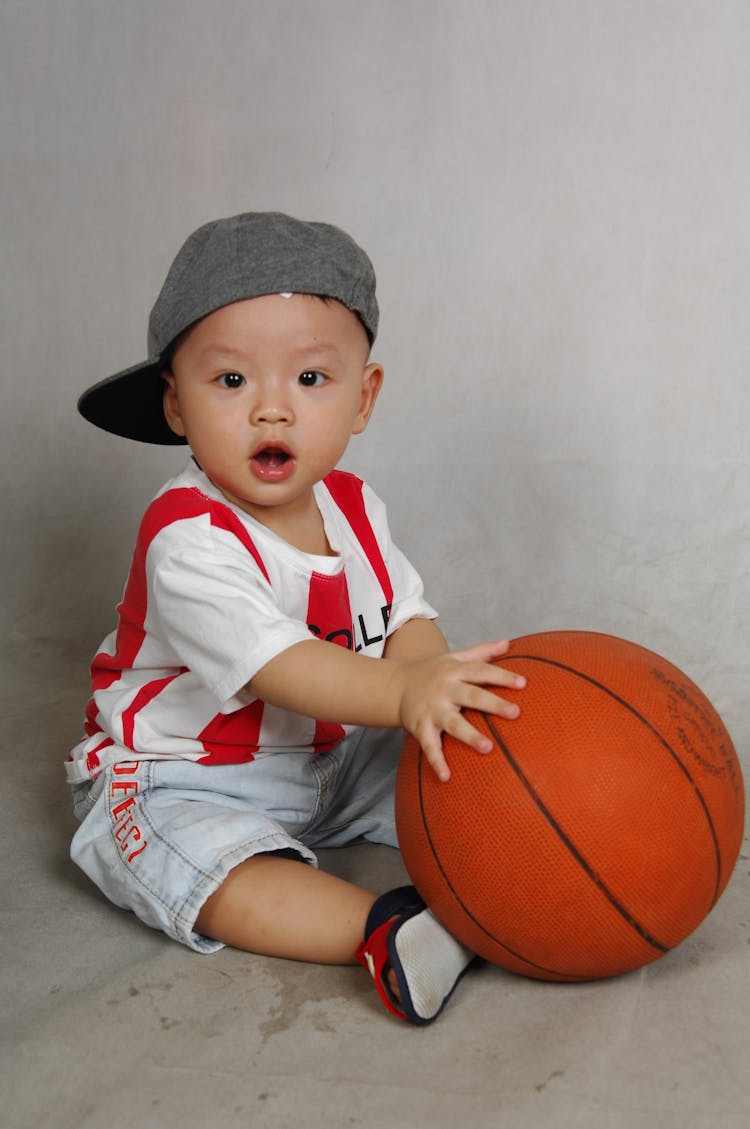 Toddler Sitting On The Floor Holding Basketball