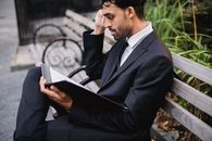 一名身着西装的男子坐在公园长凳上，专注地阅读着文件夹