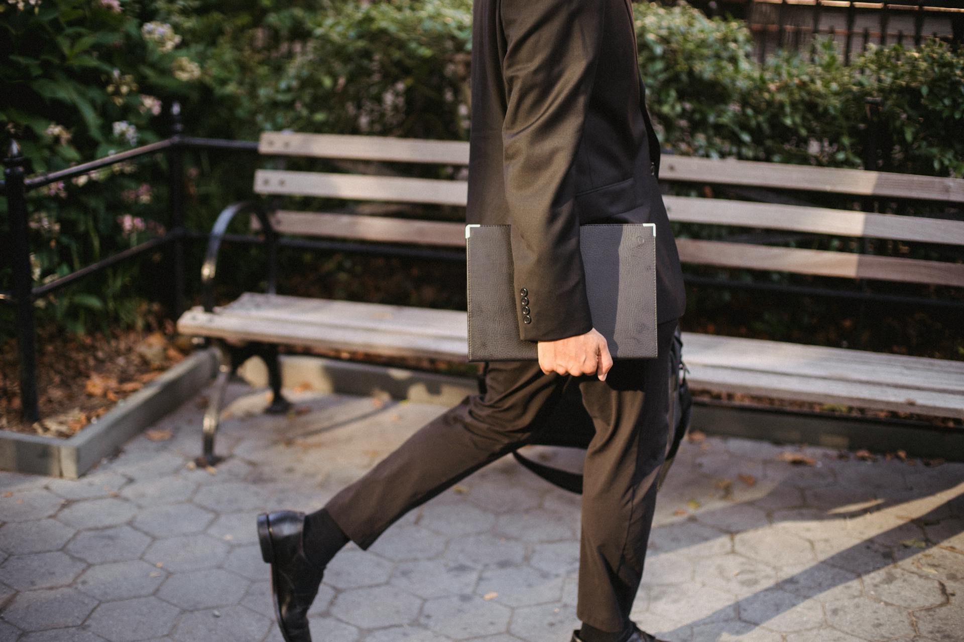 An anonymous man in a black suit walks in a park holding a portfolio, showcasing a professional urban lifestyle.