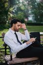 一名留着胡须、身穿正装的男子若有所思地坐在公园的木凳上读书