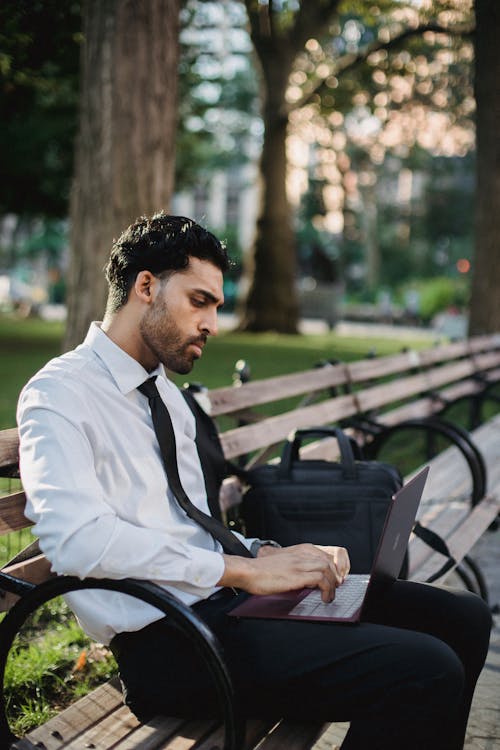 Free A Man in a White Long Sleeves Using a Laptop While Sitting on a Wooden Bench Stock Photo