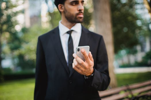Businessman in black suit holding smartphone outdoors looking thoughtful.