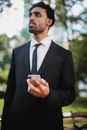 白天在公园里，一位穿着西装、拿着手机的职业男子