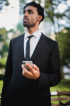 白天在公园里，一位穿着西装、拿着手机的职业男子