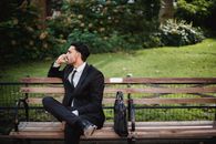 一名衣冠楚楚、身着黑色西装的男子正坐在公园长凳上打电话