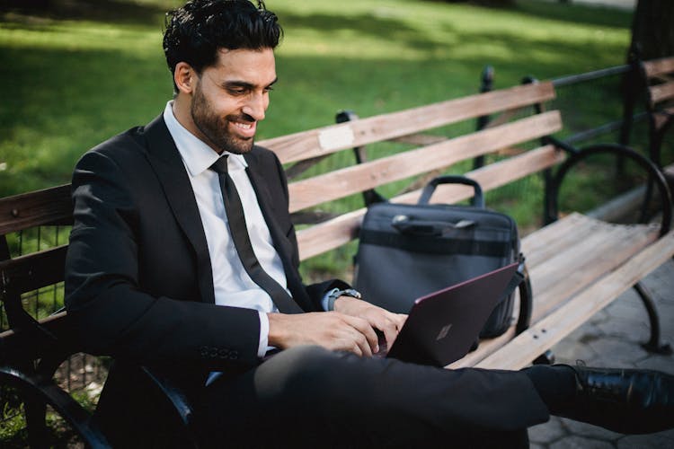 Man In Black Suit Sitting On Bench Using Laptop