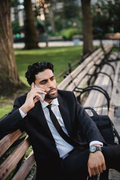 Man in Black Suit Sitting on Bench Speaking on  Phone