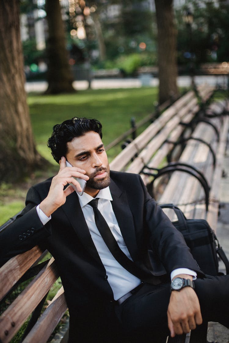 Man In Black Suit Sitting On Bench Speaking On  Phone