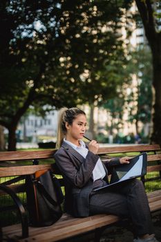 一位身穿灰色西装的职业女性在公园里用平板电脑思考和规划