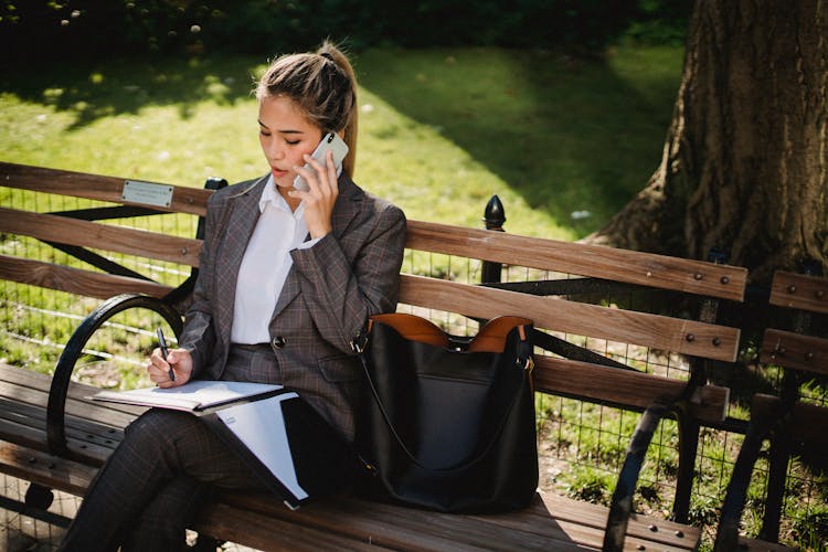 Young Woman In Business Suit Sitting On Bench In Park