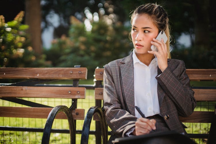 Business Woman In Suit On Park Bench Talking On Mobile