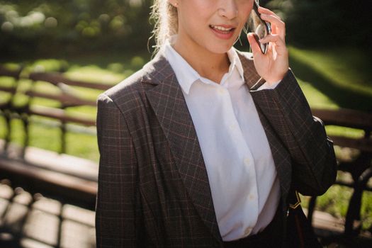 一位女商人在阳光明媚的公园里边散步边打电话