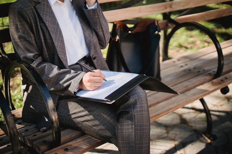 Woman Sitting On A Park Bench Filing Out Paperwork