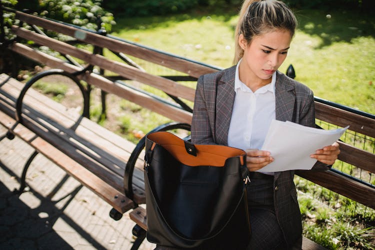 Businesswoman Sitting On A Park Bench And Looking At Documents 