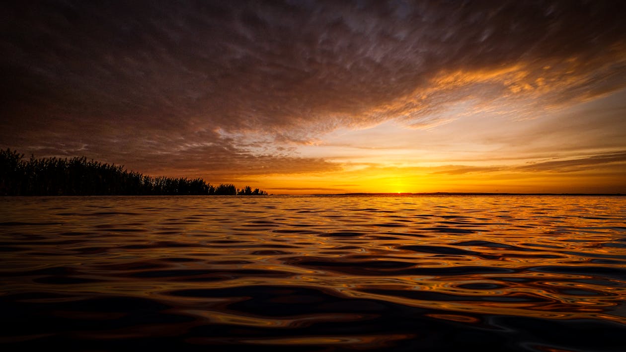 Photograph of a Body of Water Under a Cloudy Sky During Sunset