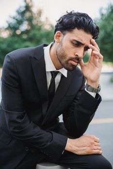 一名男子身穿黑色西装，在户外沉思