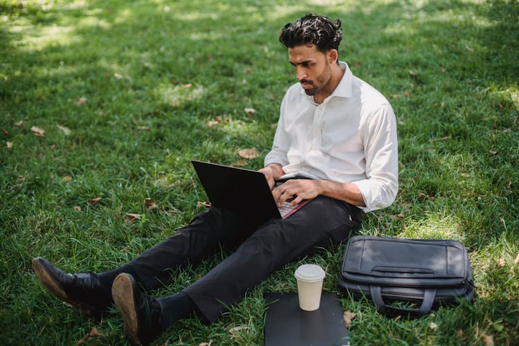 A Businessman Sitting On Grass While Using His Laptop