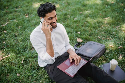 Free A Businessman Sitting on Grass while Having a Phone Call Stock Photo