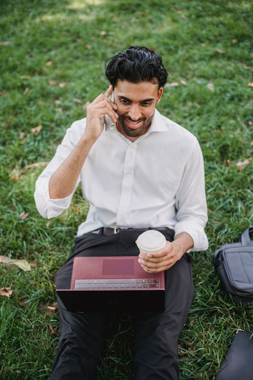 A Businessman Sitting on Grass while Having a Phone Call