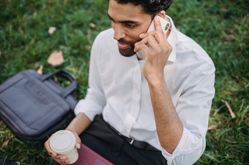Free A Businessman Having a Phone Call while Holding a Disposable Cup Stock Photo