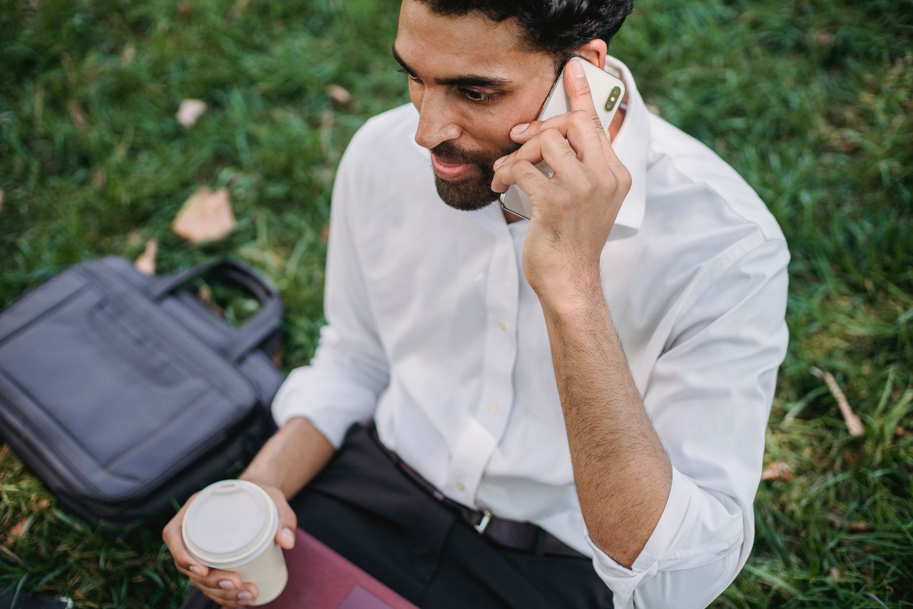Professional man in a park using smartphone, holding coffee, working remotely outdoors.