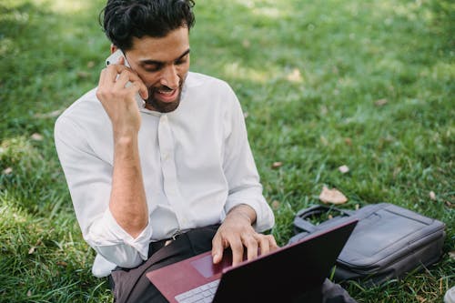 Free A Businessman Having a Phone Call while Using His Laptop Stock Photo