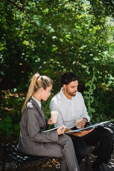Two professionals engaged in a business discussion while enjoying coffee in a natural outdoor setting.