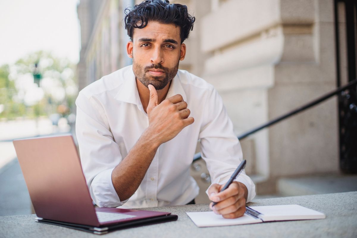 Homem escrevendo em um caderno enquanto pensa sobre um projeto